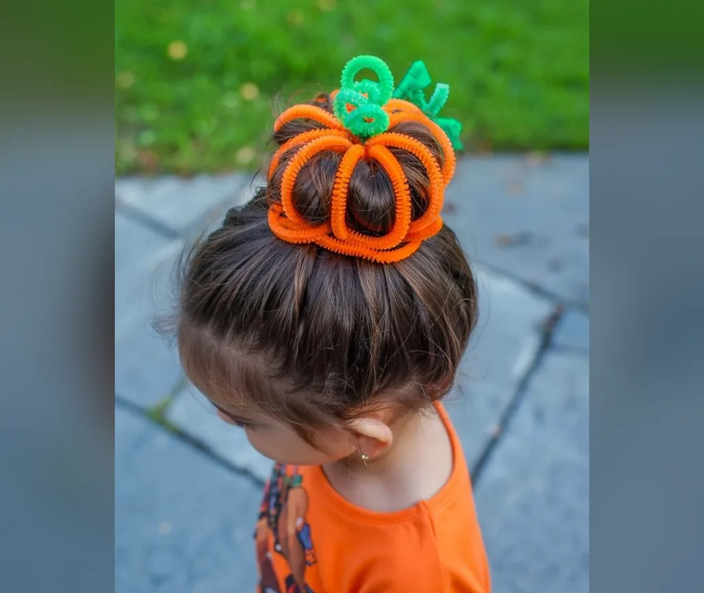 Toddler with a single orange pumpkin top bun outdoors, gentle halloween hairstyles for girls
